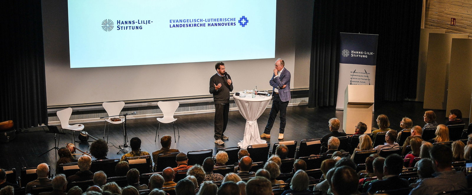 Zwei Menschen diskutieren auf einer Bühne vor Publikum