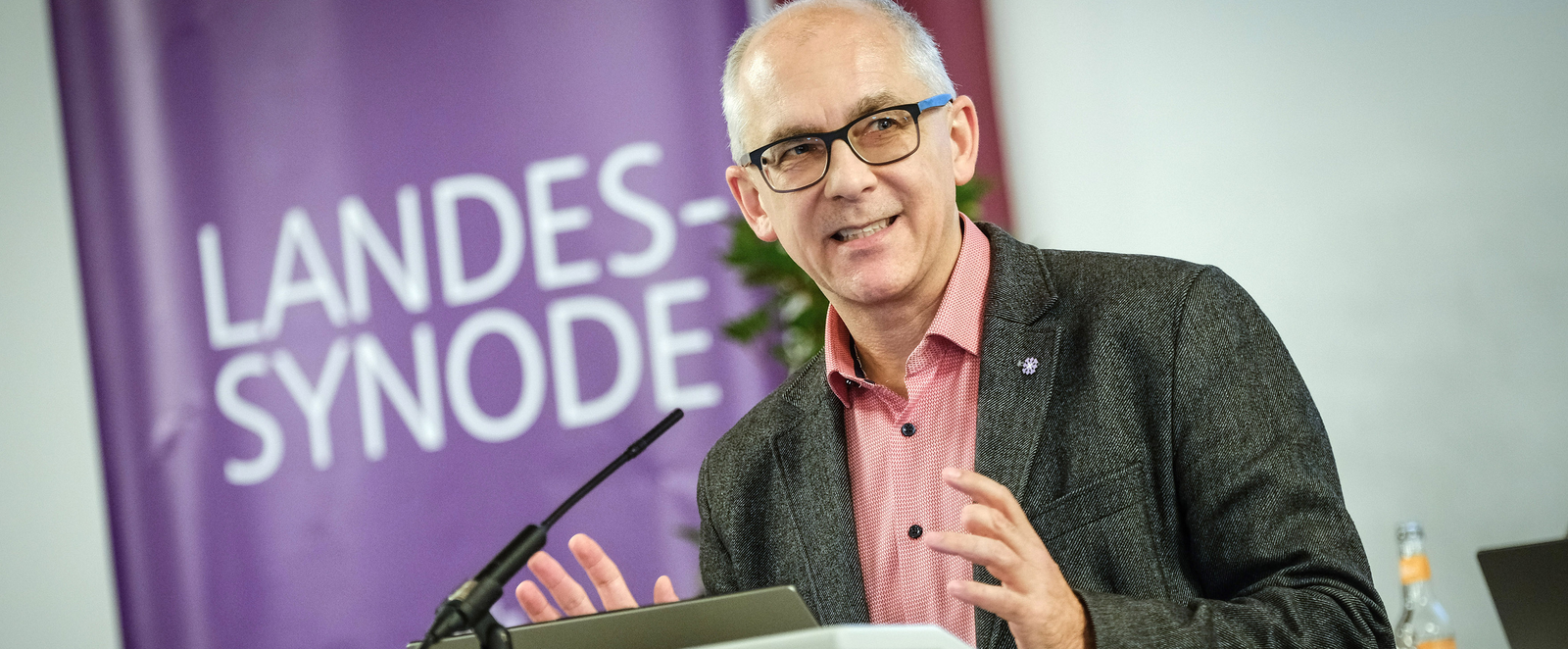 Eine männlich lesbare Person steht an einem Rednerpult und spricht.