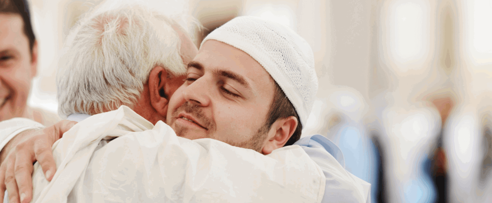 Zwei in weiß gekleidete Männer umarmen sich und lächeln dabei.