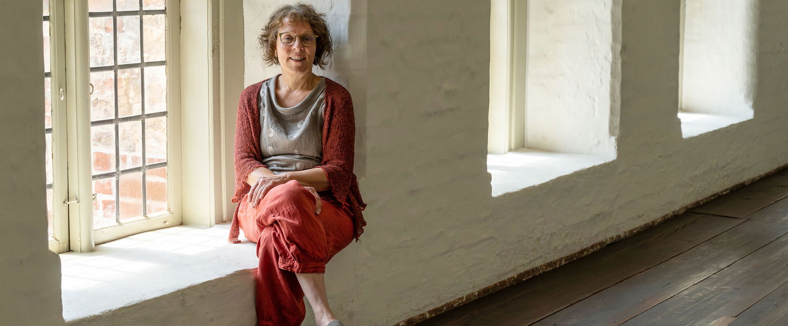 Eine Frau sitzt in einem Fenster im Kreuzgang eines Klosters.