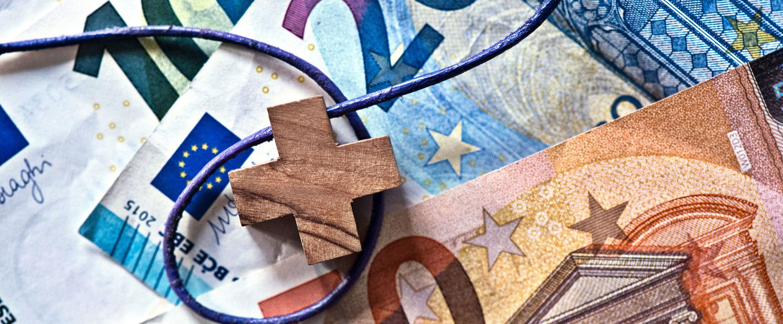 Auf Euro-Banknoten liegt ein Holzkreuz an einer Kette.