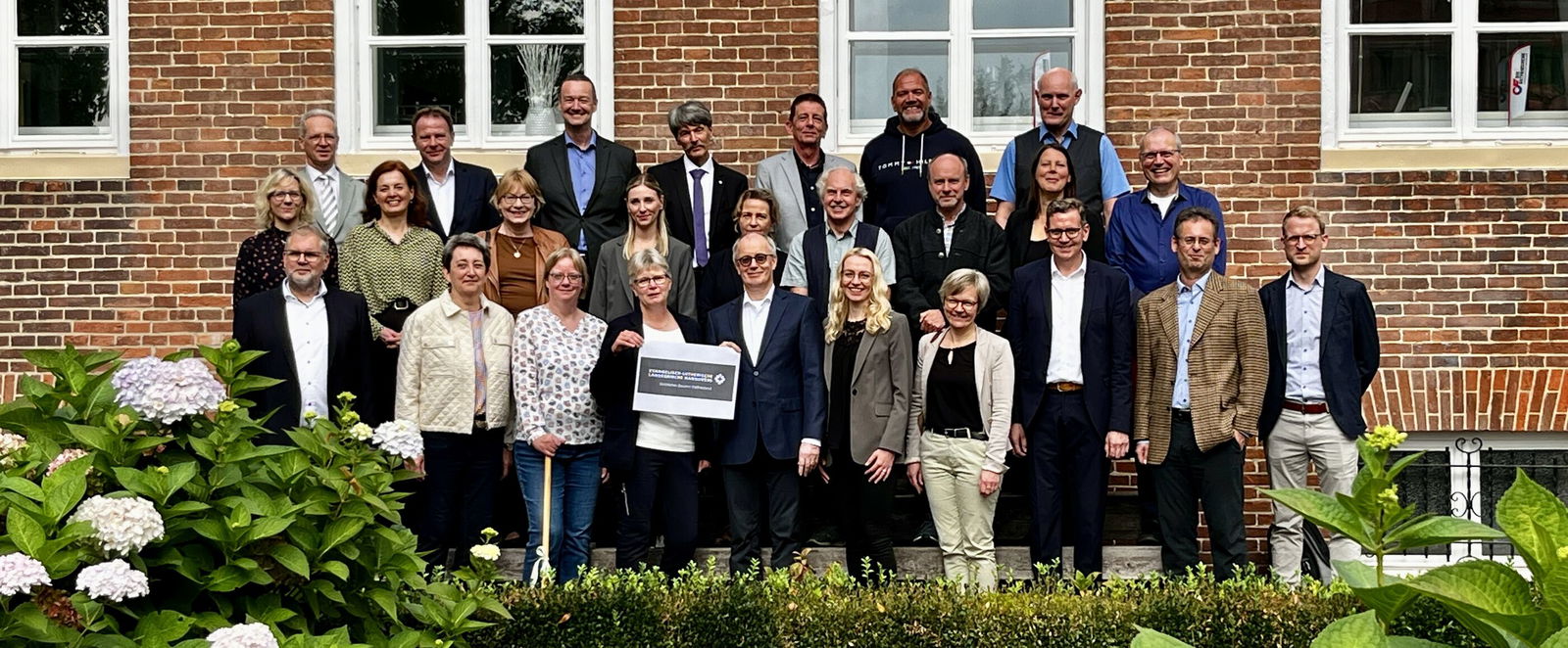 Ein Gruppenbild mit mehr als 20 Personen vor einem Haus mit roter Klinkerwand.