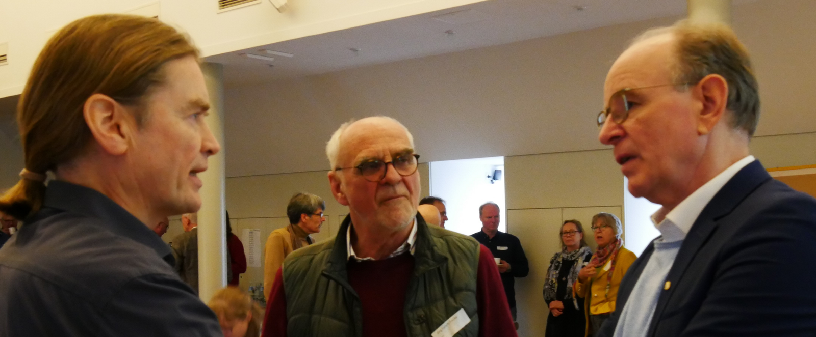 Drei Personen stehen zusammen im Gespräch. Die mittlere hält eine Kaffeetasse in Händen.