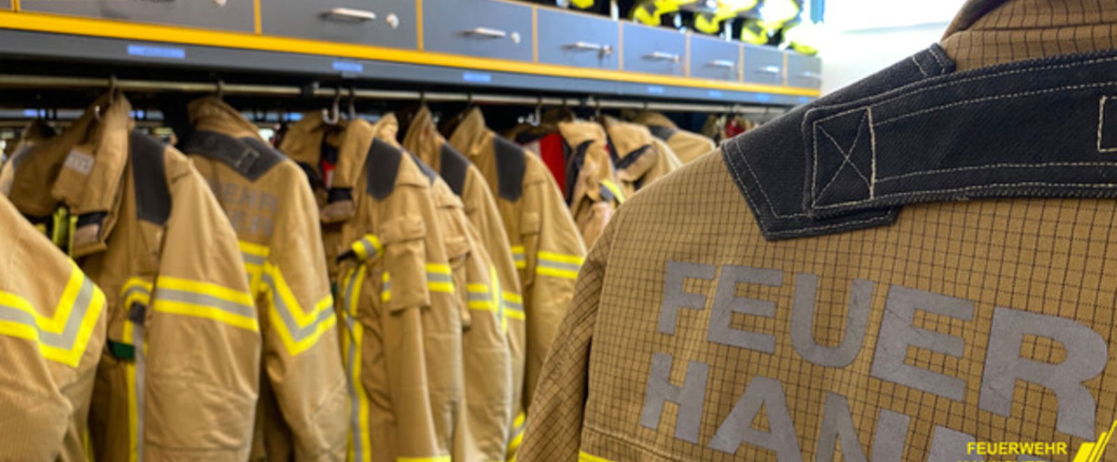 Gelbe Feuerwehrjacken hängen in einer Reihe in einem Schrank.