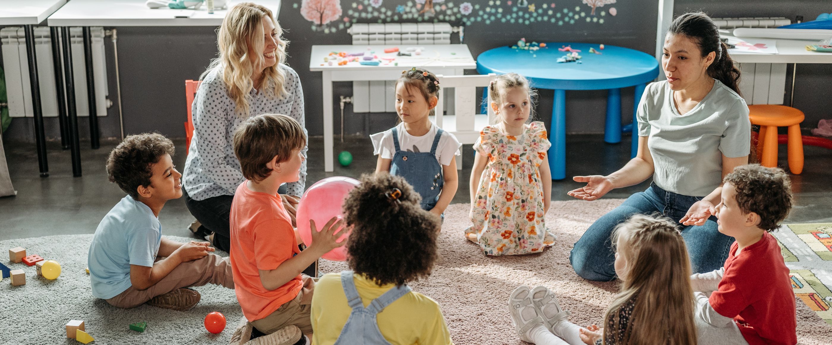 Ein Gruppe von Kindern sitzt mit zwei Erzieherinnen im Kreis.