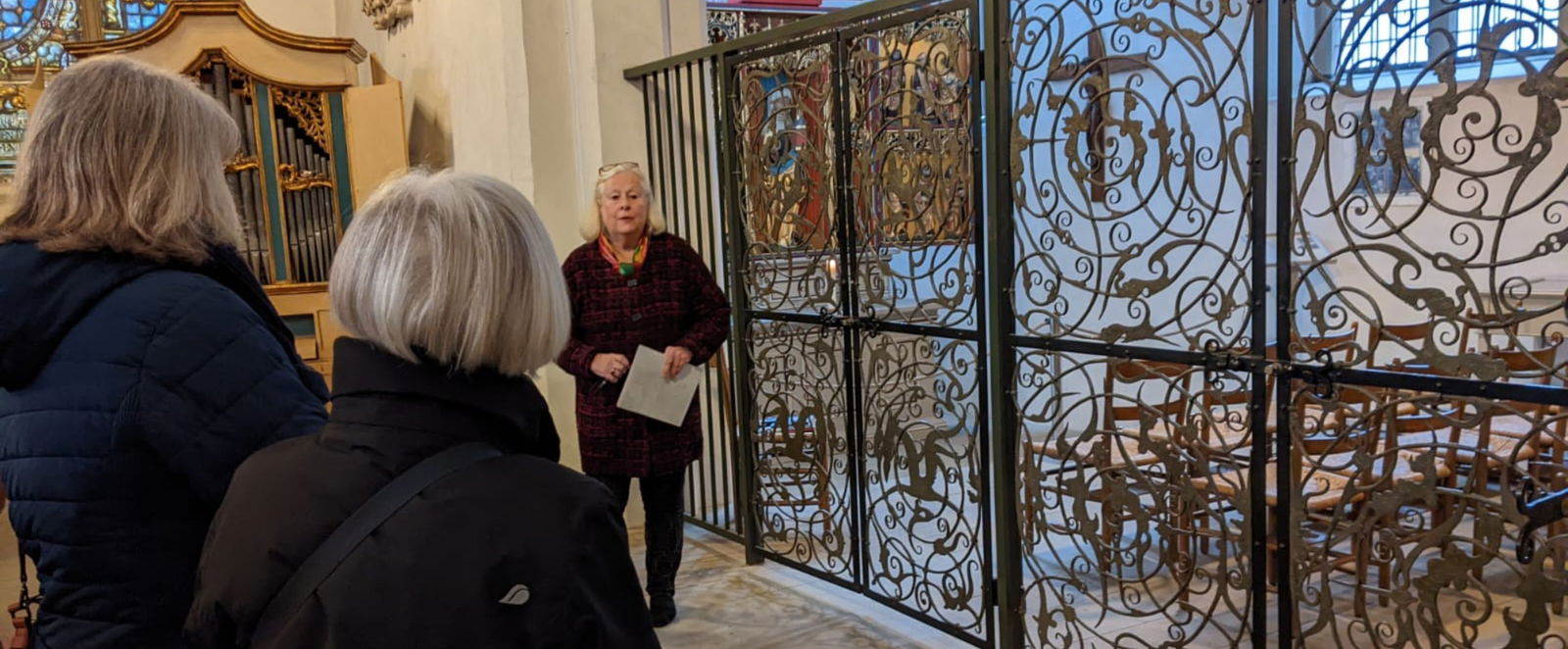 Eine Gruppe Menschen steht um eine Frau in einer Kirche. Im Hintergrund ist ein Kreuz und eine Orgel.