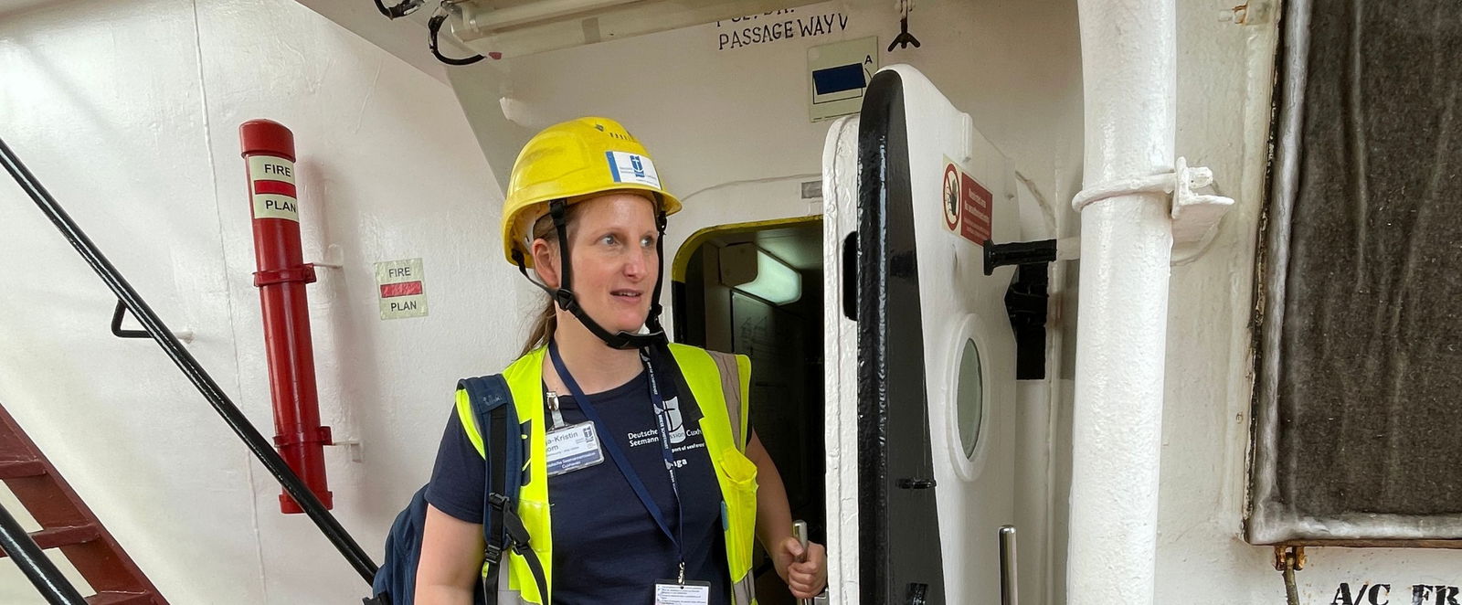 Eine weiblich gelesene Person steht mit Helm und Warnweste auf einem Schiffsdeck.