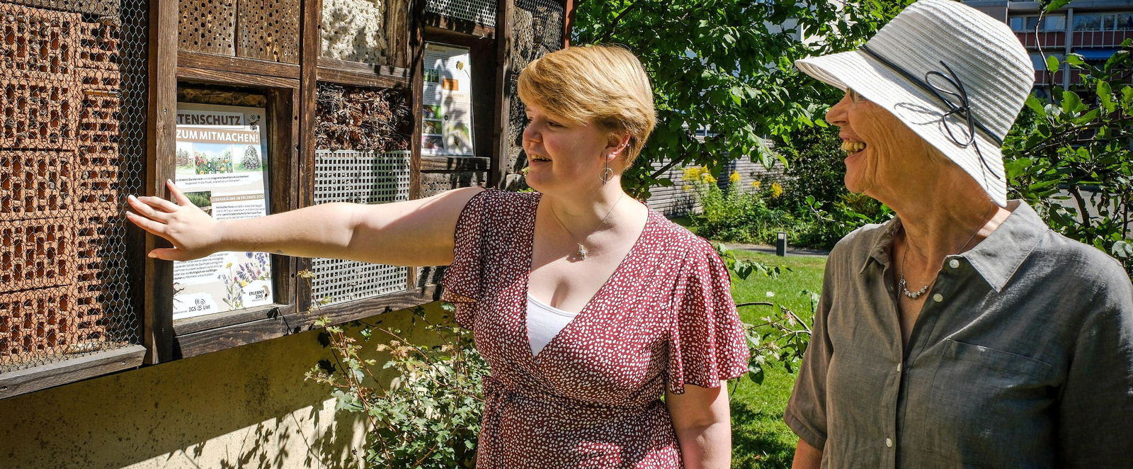 Zwei Menschen stehen im Grünen vor einem Insektenhotel. 