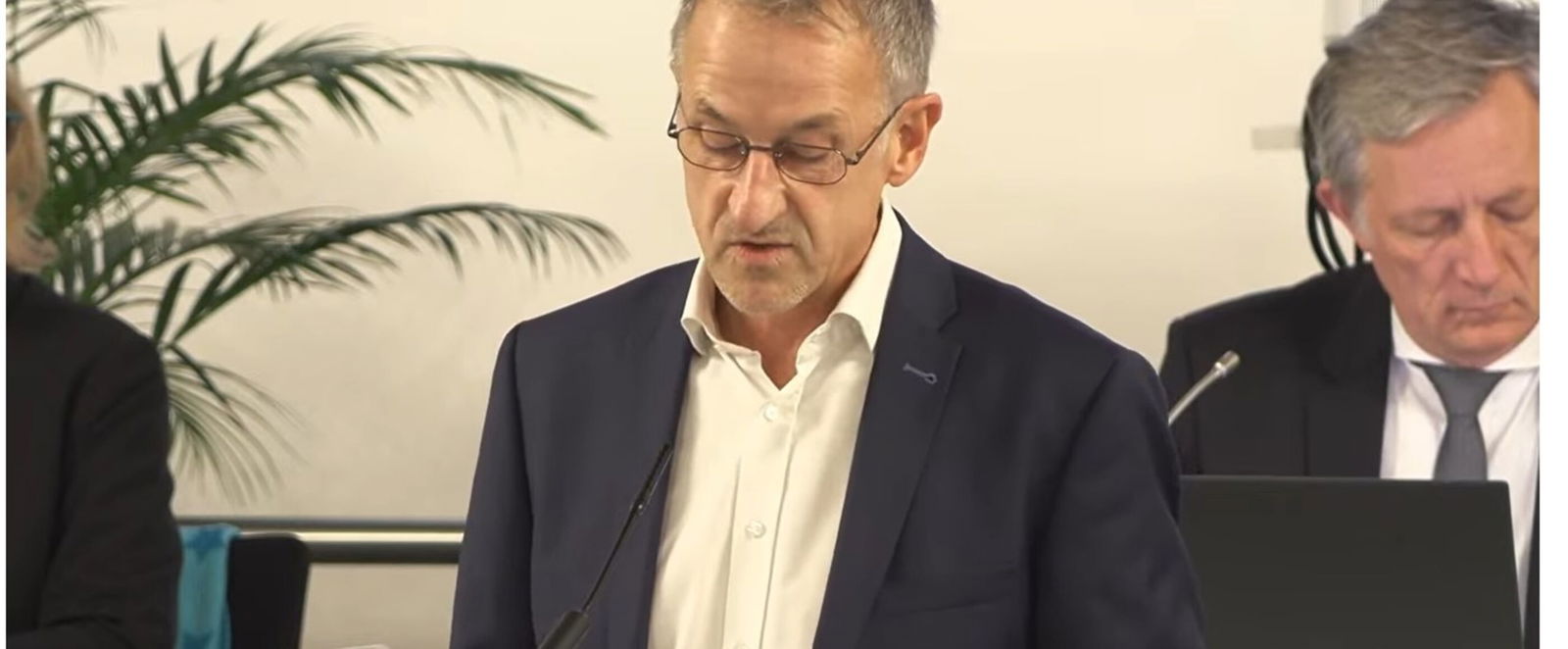 Eine männlich gelesene Person mit kurzem haar in weißem Hemd und Sakko.