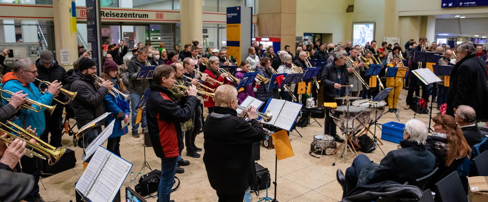 Menschen spielen Blasinstrumente in einer Bahnhofshalle.