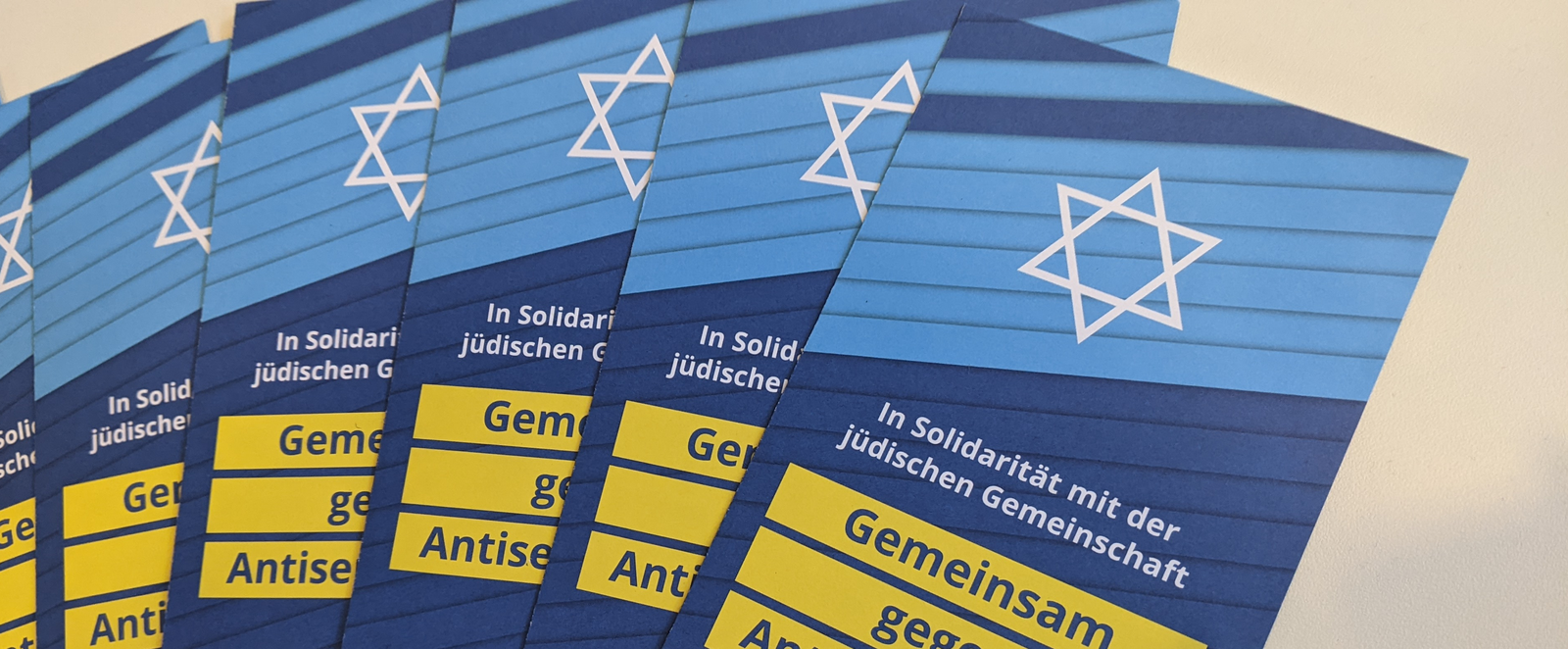 Mehrere Flyer liegen in Reihe. Er zeigt einen weißen Davidstern auf blauem Untergrund. Darunter steht: In Solidarität mit der jüdischen Gemeinschaft - Gemeinsam gegen Antisemitismus