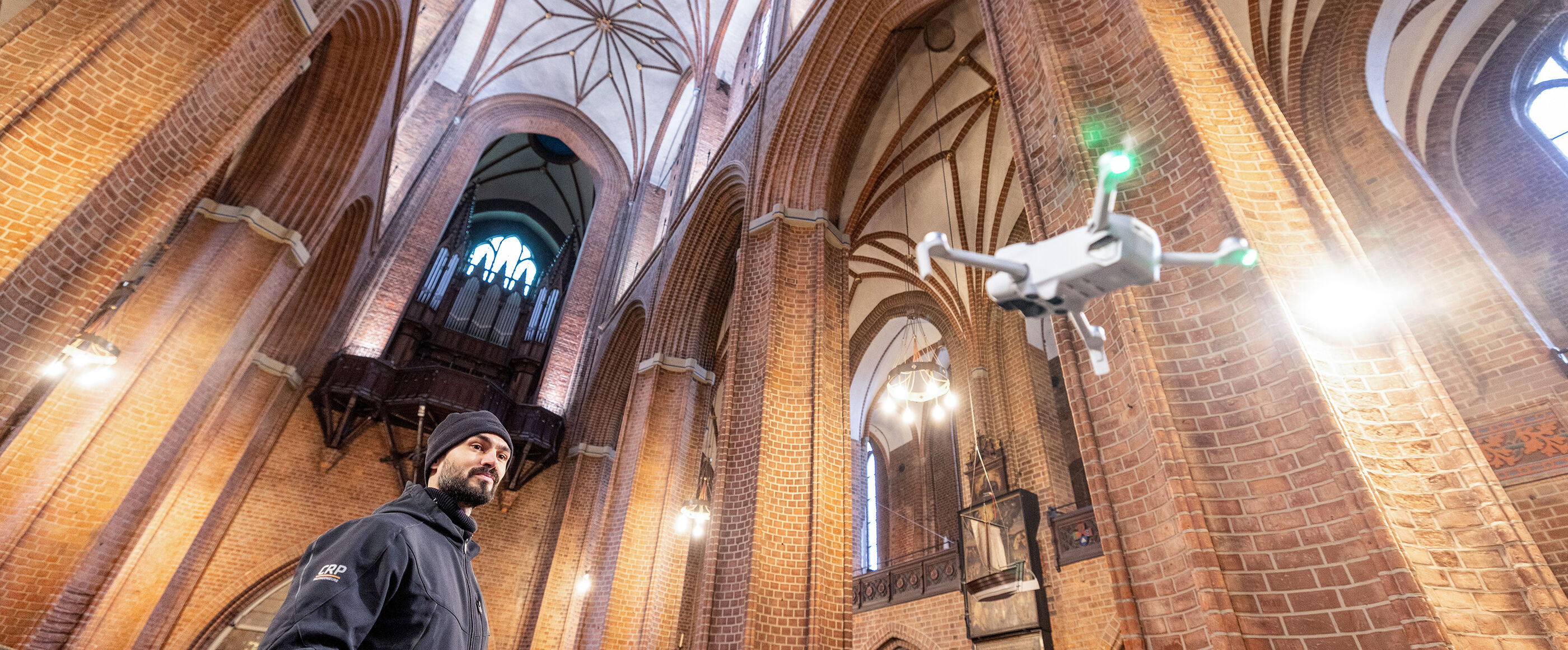 Eine als Mann lesbare Person lässt eine Drohne in einer Kirche fliegen.