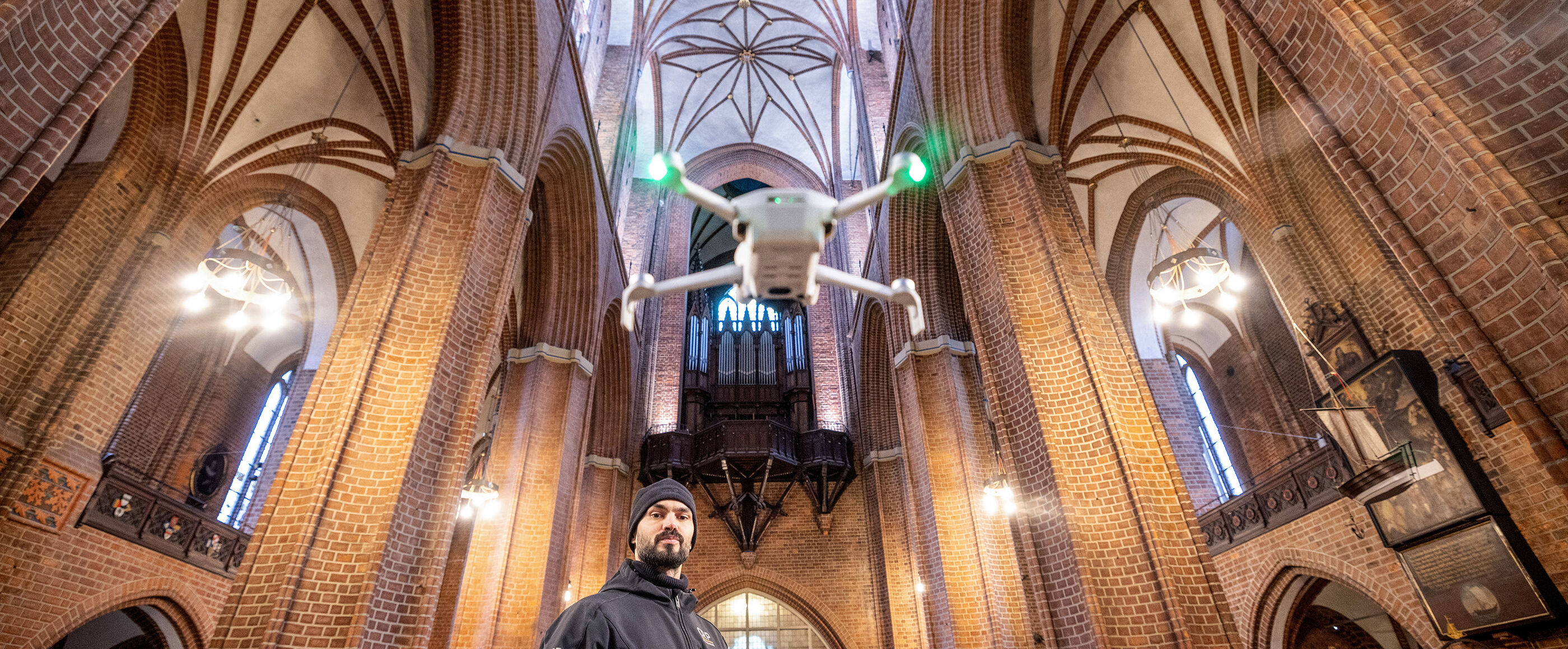 Eine als Mann lesbare Person lässt eine Drohne in einer Kirche fliegen.