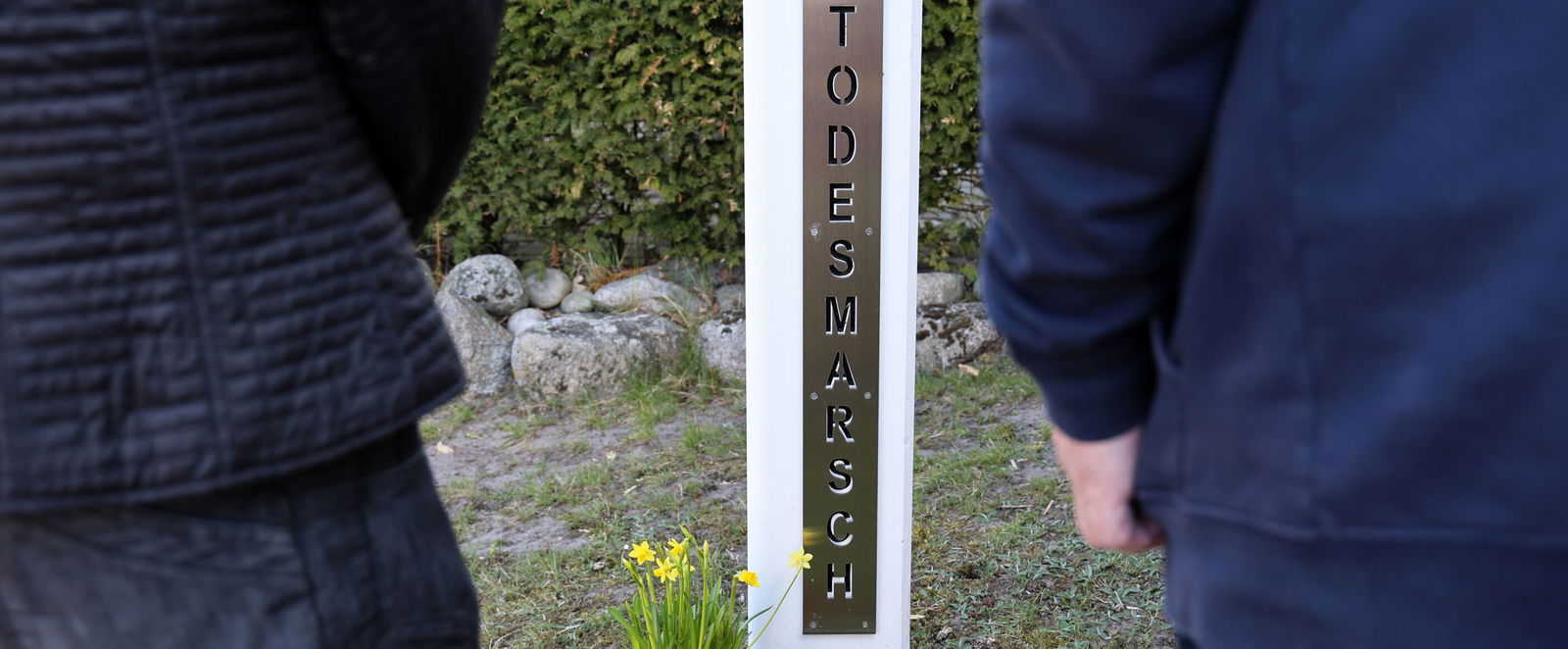 Zwei Menschen stehen vor einer Stele, auf der Todesmarsch steht.