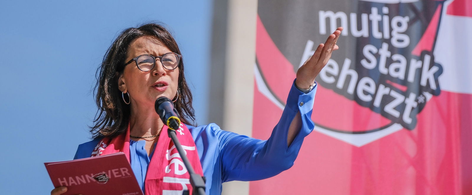 Eine weiblich zu lesende Person spricht in ein Mikrofon.