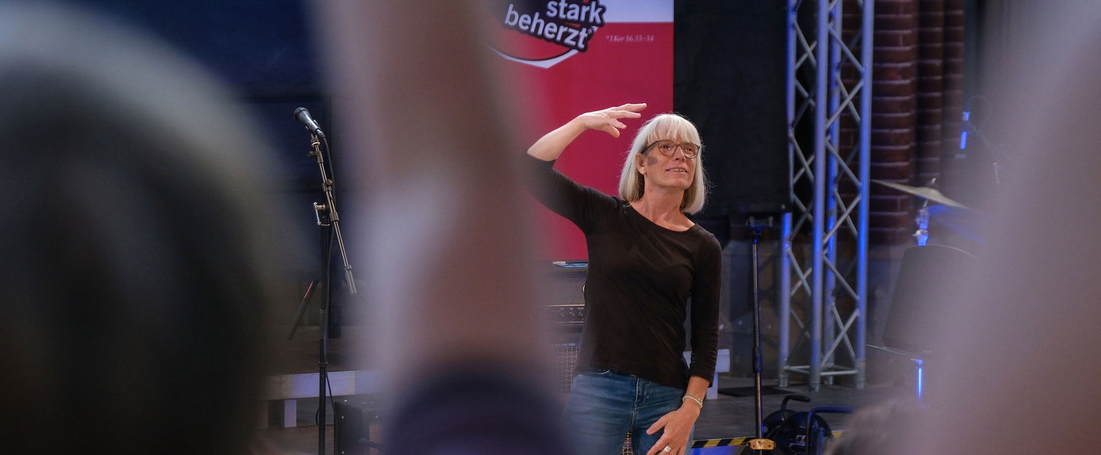 Eine weiblich zu lesende Person steht auf einer Bühne und gebärdet ein Lied.