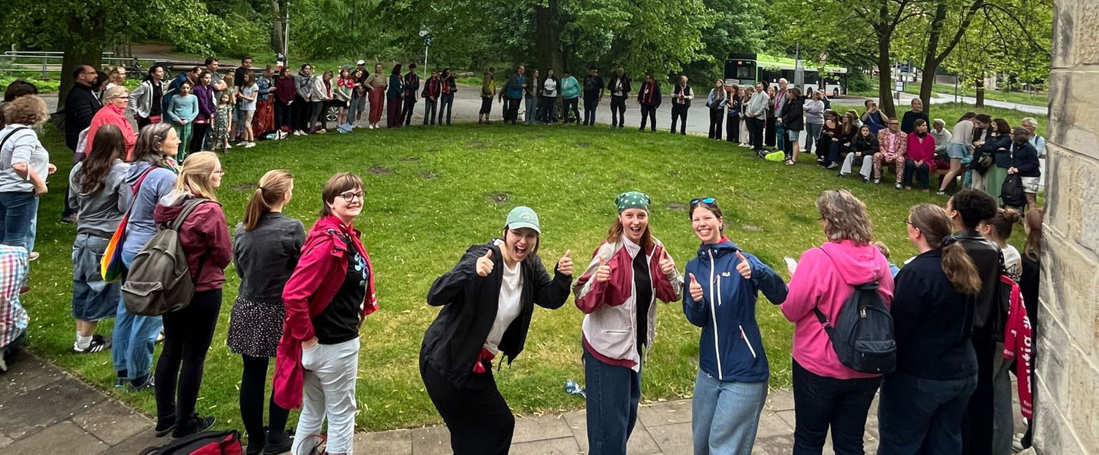 Eine große Gruppe Jugendlicher steht auf einer Wiese im Kreis.
