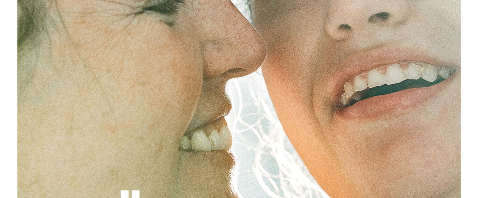 Zwei Personen in sehr naher Aufnahme, die Köpfe liegen aneinander, beide lächeln leicht. Darunter steht: Glück inklusive. 