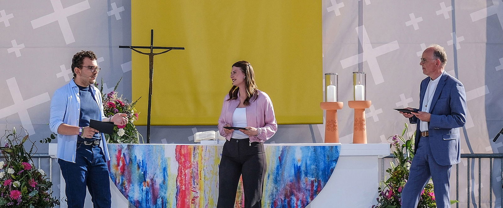 Zwei als Männer und eine als Frau lesbare Personen im Gespräch auf einer großen Bühne.