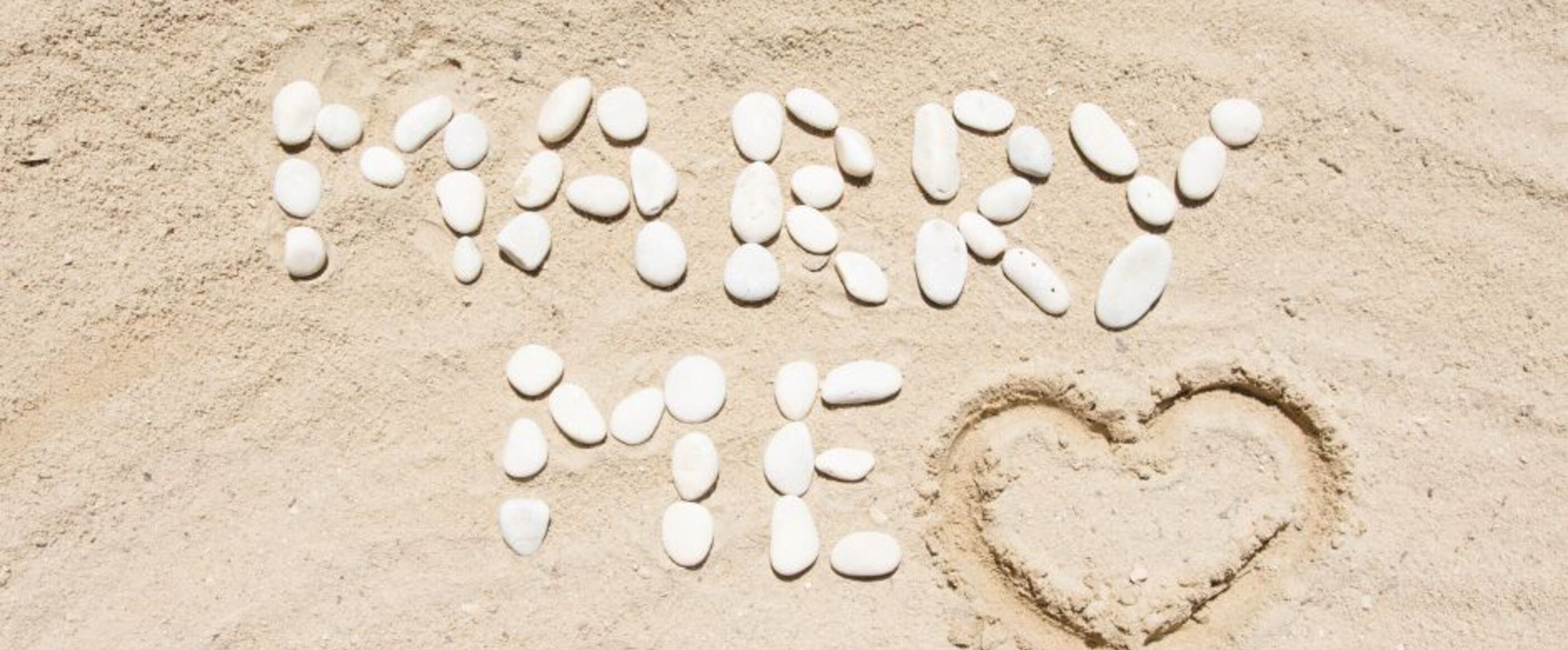 Im Sand liegen weiße Muschlen und bilden die Worte "Marry me" und ein Herz.