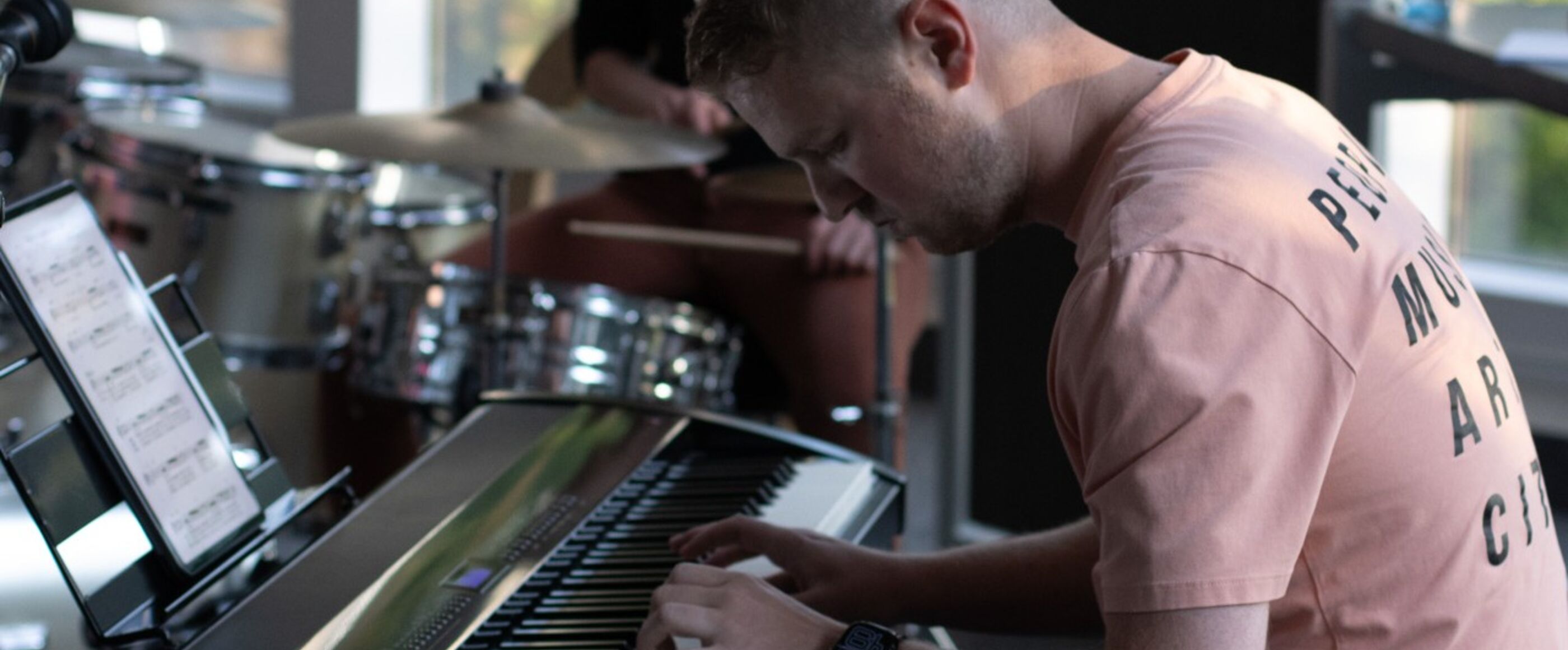 Eine männlich gelesene Person in orange-rosa Shirt sitzt an einem Keyboard.
