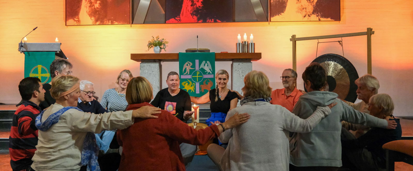 Eine Gruppe von Menschen sitzt im Kreis, jeder Person legt der rechts von ihr sitzenden die Hand auf die Schulter.