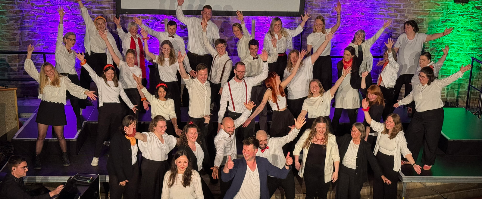 Etwa zwei Dutzend Menschen in dunklen Hosen und weißen Hemden stehen zusammen und heben die Hände.