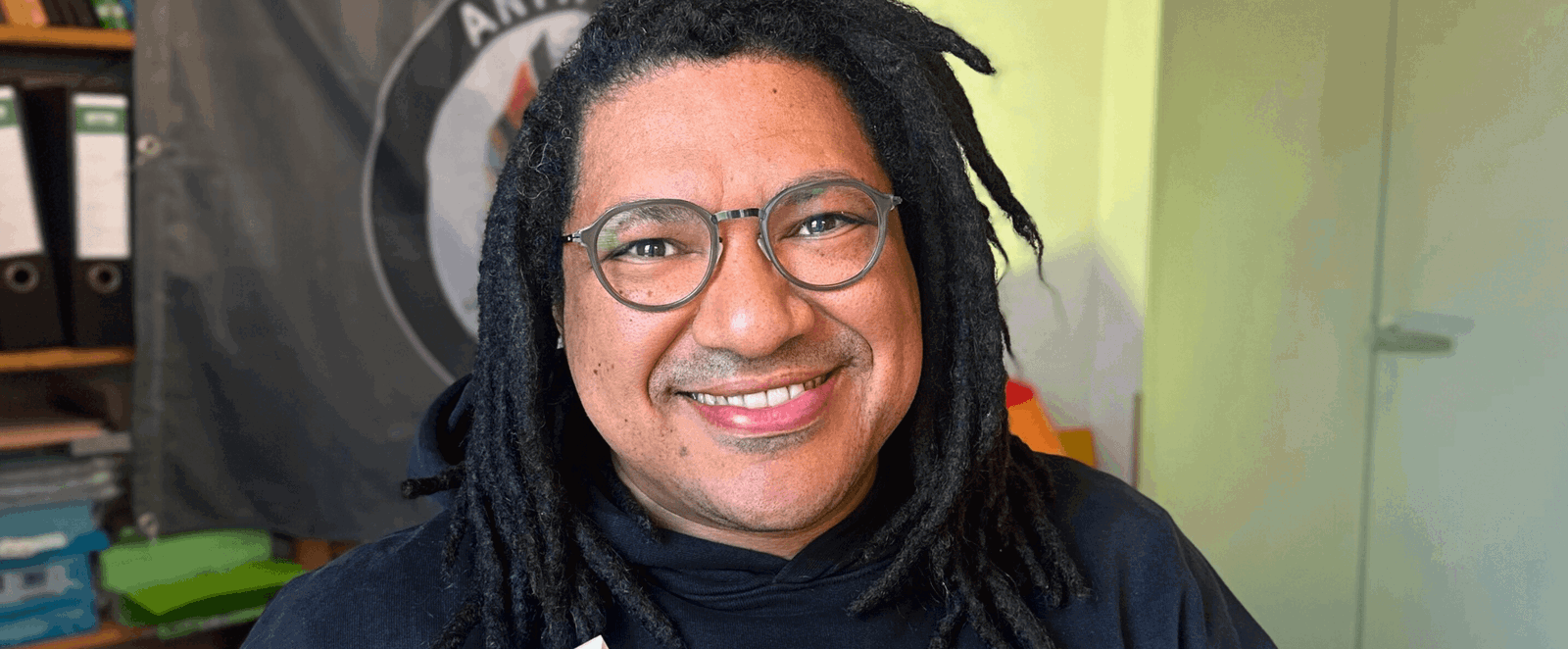 Eine Person dunkler Hautfarbe mir Brille hält ein Buch in Händen, der Titel: Gemeinsam anders.