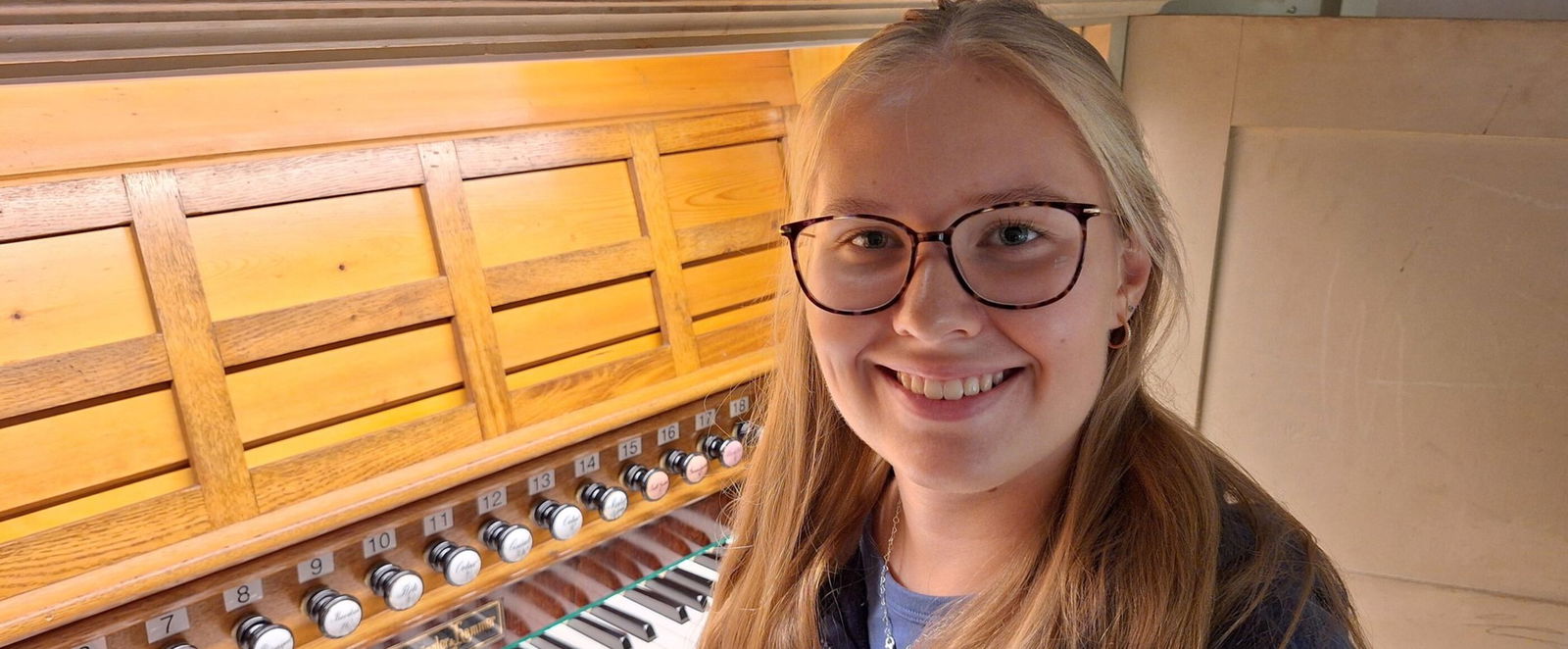 Eine weiblich gelesene, junge Frau mit Brille sitzt an einer Orgel.