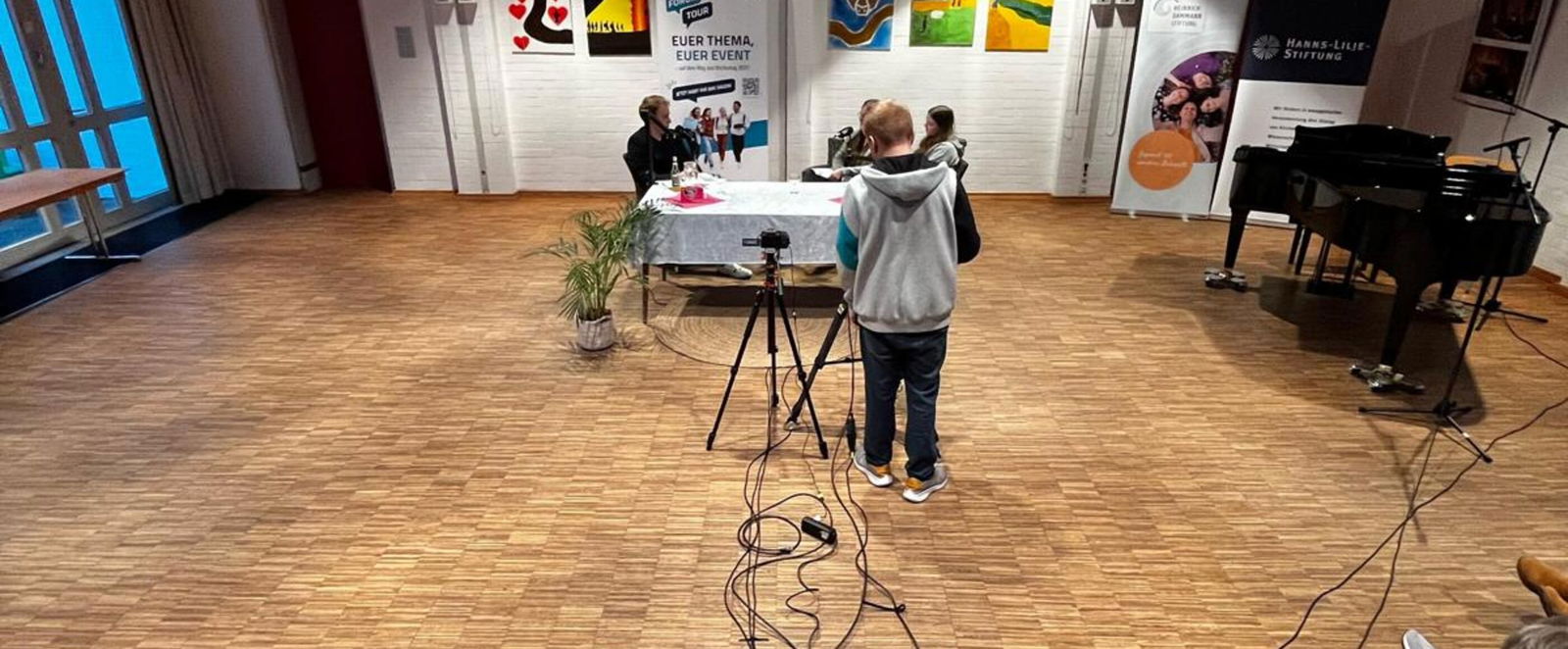 Zwischen zwei Tischen liegen Kabel, auf den Tischen Mikros und Laptops und technische Geräte.