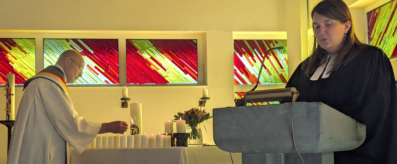 Eine männlich gelesene Person in weißem Talar und eine weiblich gelesene in schwarzem Talar in einer Kirche.