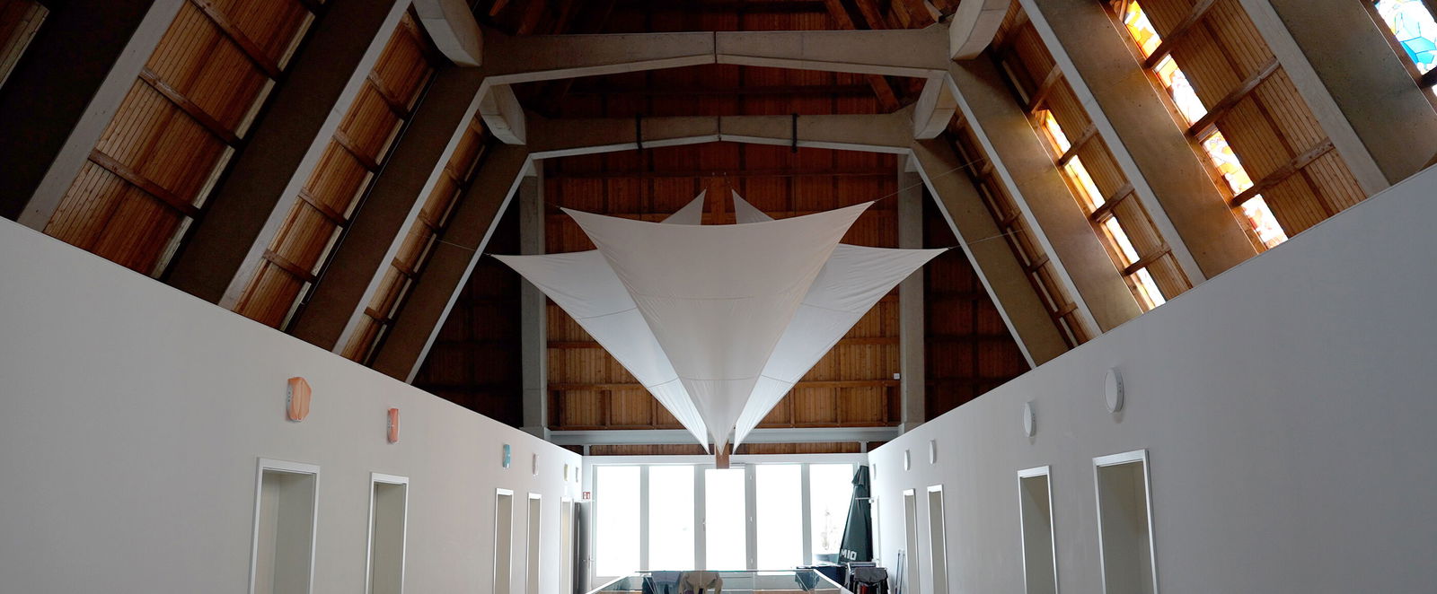 Blick in das Schiff einer Kirche, in das weiße Wände gezogen sind und Tücher unter der Holzdecke hängen.