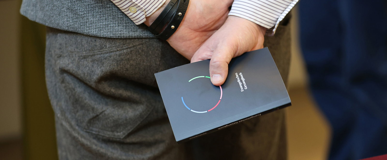 Jemand hält ein Erprobungsgesangbuch hinter dem Rücken in den Händen