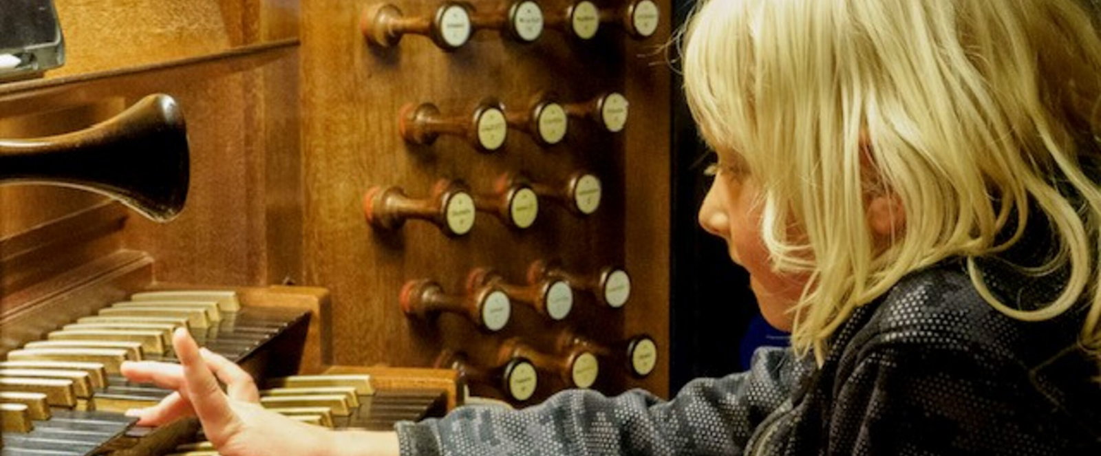 Ein blondes Kind spielt mit einer Hand auf einer Orgel-Tastatur.