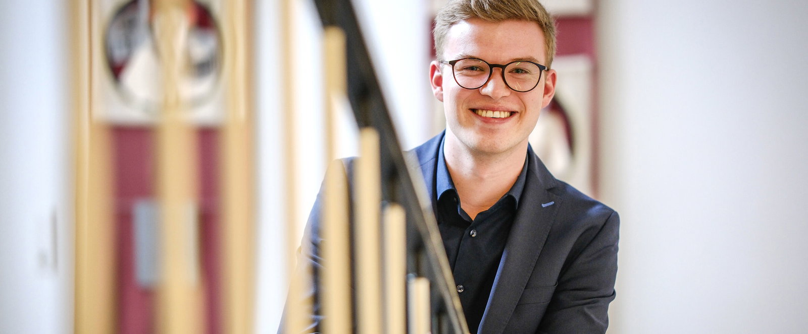Eine junge als Mann lesbare Person steht an einem Geländer.
