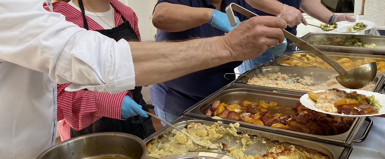 vier pPersonen verteilen aus großen Töpfen Essen