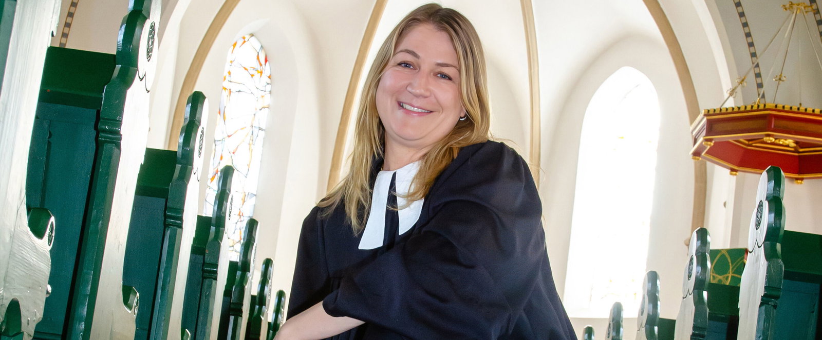 Eine als Frau lesbare Person hockt im Talar in einer Kirche