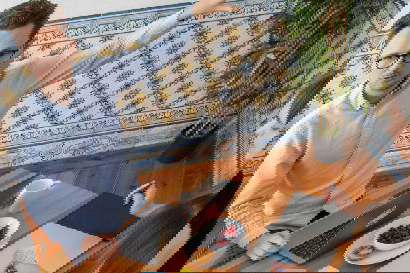 Eine Gruppe von fünf Menschen, die um einen Tisch sutzen. Notizbücher und Post-its. Ein Meeting-Raum mit Holzmöbeln, Sofa, Tapete und Grünpflanze. 