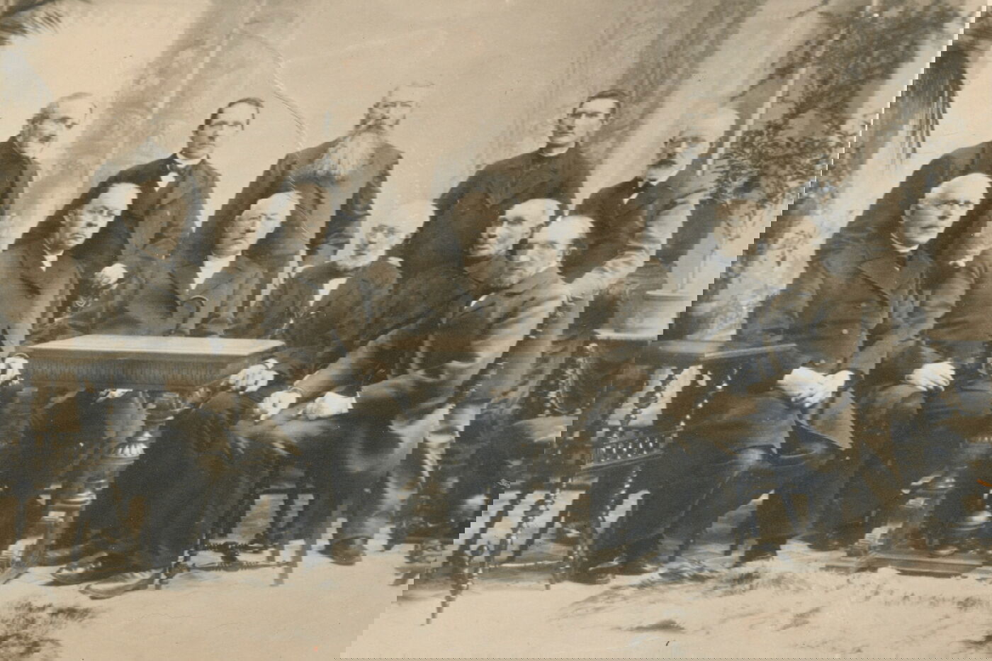 Das Bild zeigt eine historische Aufnahme von zehn männlich lesbaren Personen, die sich in zwei Reihen hinter einem Tisch postiert haben für das Foto; sie tragen dunkle Anzüge.