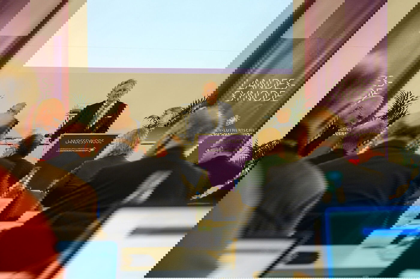 Eine männlich gelesene Person steht am Redepult vor einem Plenum.