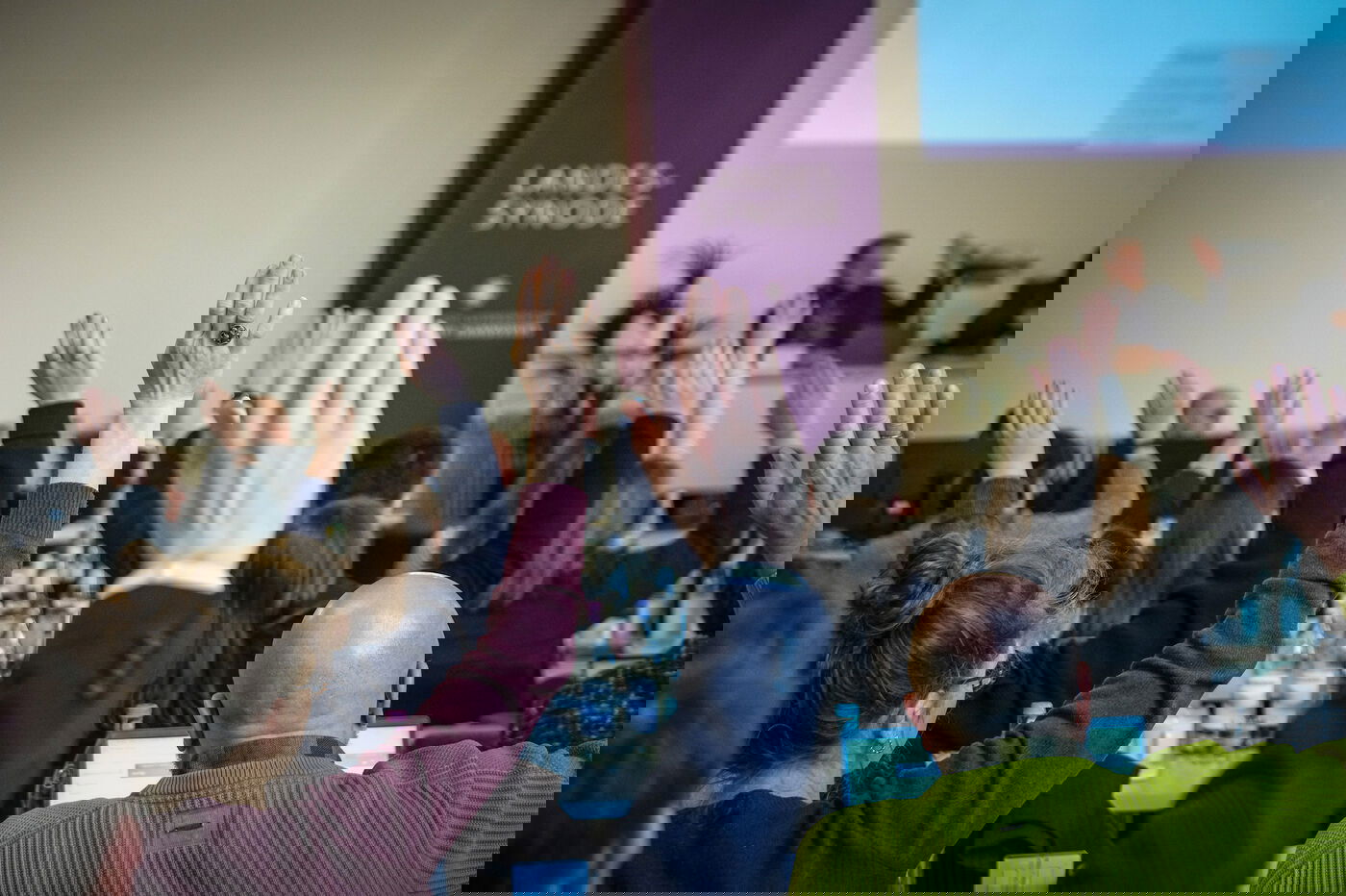 Mehrere Personen in einem Sitzungssaal heben die Hand zur Abstimmung