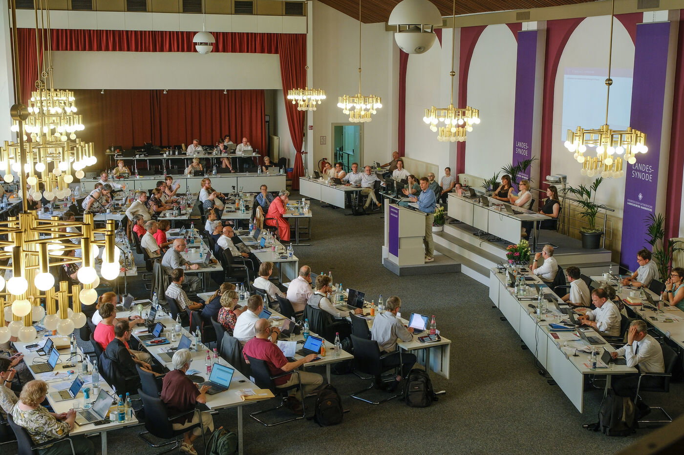 Viele Personen an Tischen in einem Sitzungssaal
