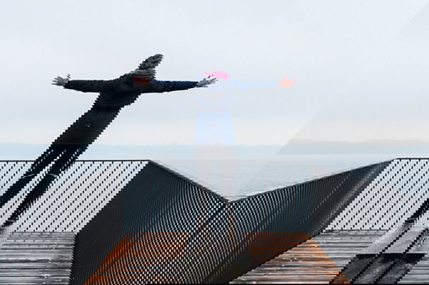 Person in Arbeitskleidung vor See mit ausgebreiteten Armen