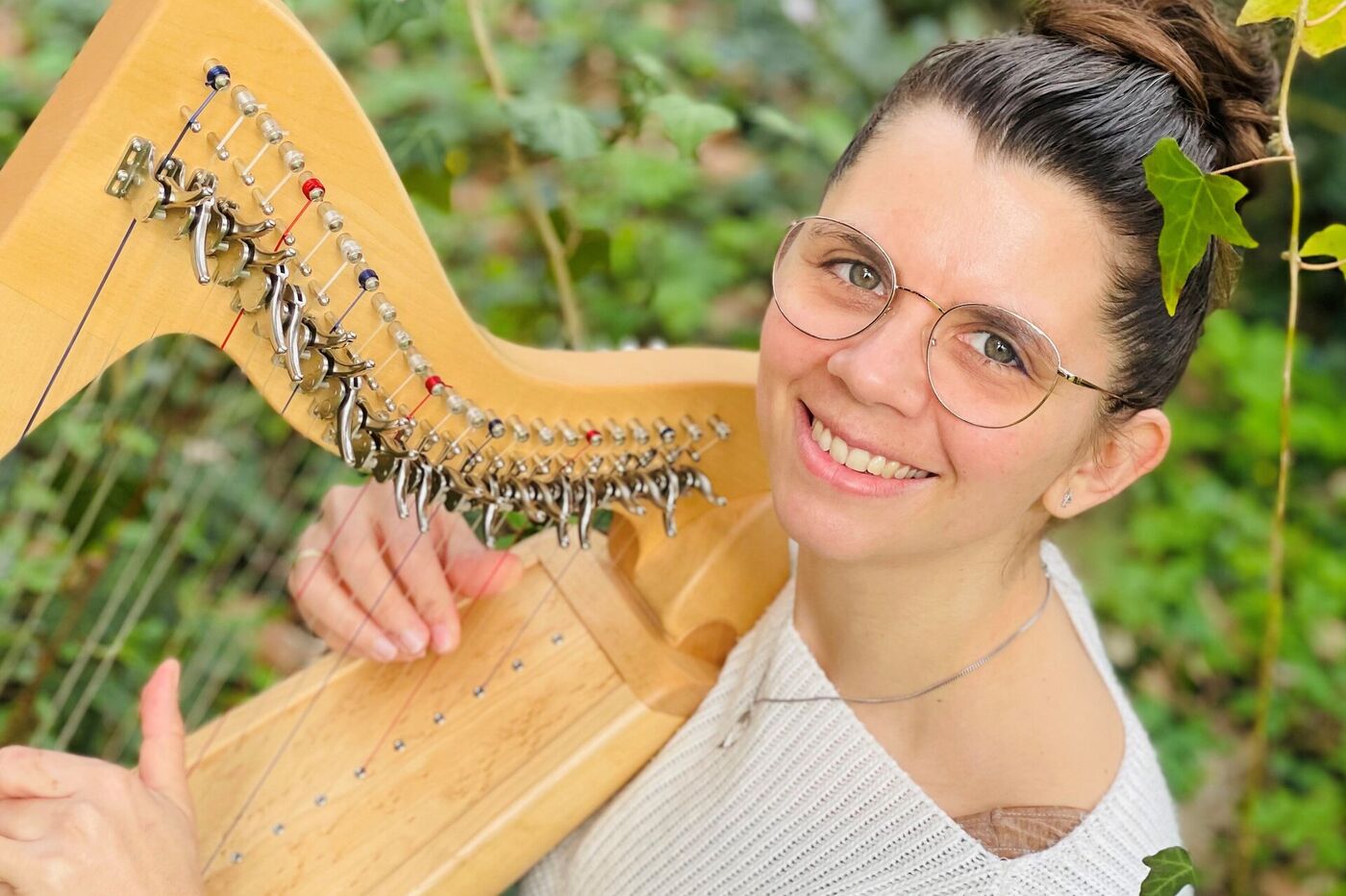 Eine als Frau lesbare Person sitzt im Grünen und spielt Harfe.