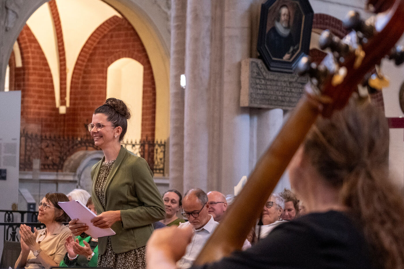 Eine als Frau lesbare Person steht in einer Kirche. Im Vordergrund ist ein Streichinstrument zu sehen.