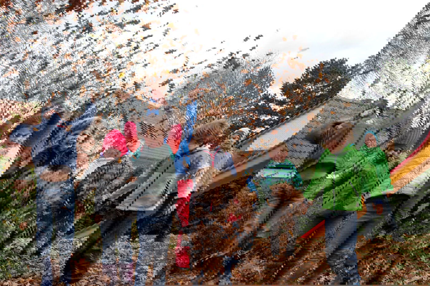 Mehrere Kinder mit Jacken werfen Laub in die Luft und freuen sich an ihrem Herabregnen.