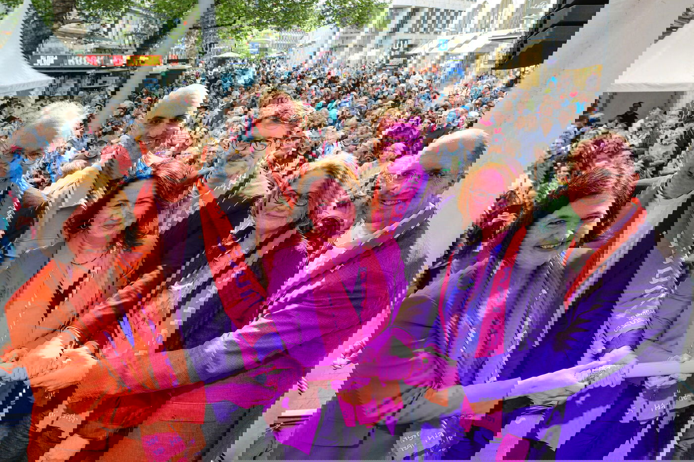 Sieben Personen stehen auf einer Bühne vor Publikum und halten alle gemeinsam einen dicken Stab. 