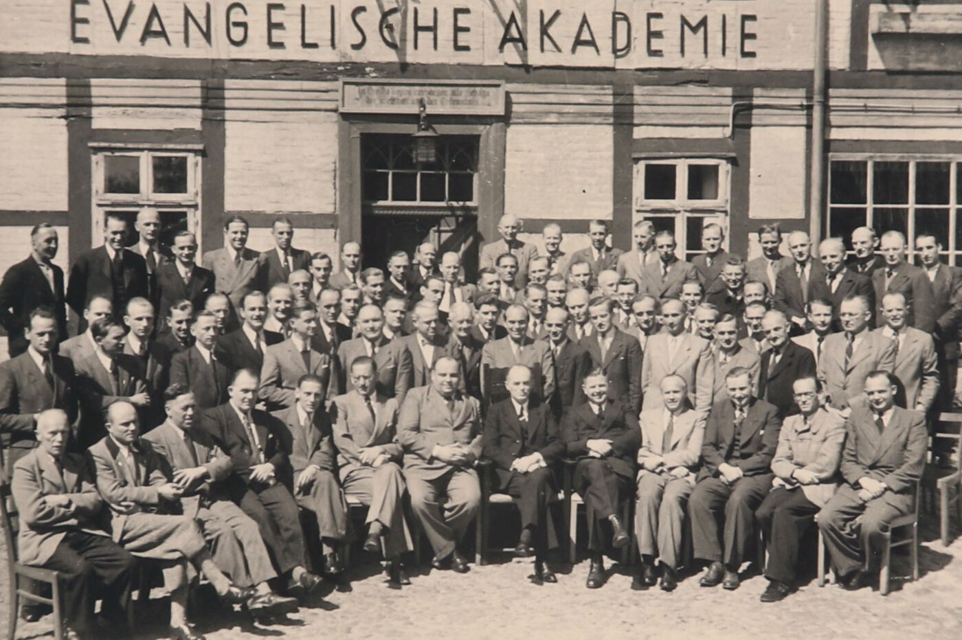 Eine historische Aufnahme mit einer Gruppe vor einem Haus mit der Aufschrift Evangelische Akademie.