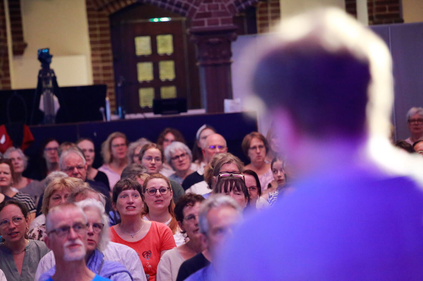 Ein Chor singt in einer Kirche. Vorn ist unscharf der Chorleiter zu sehen.
