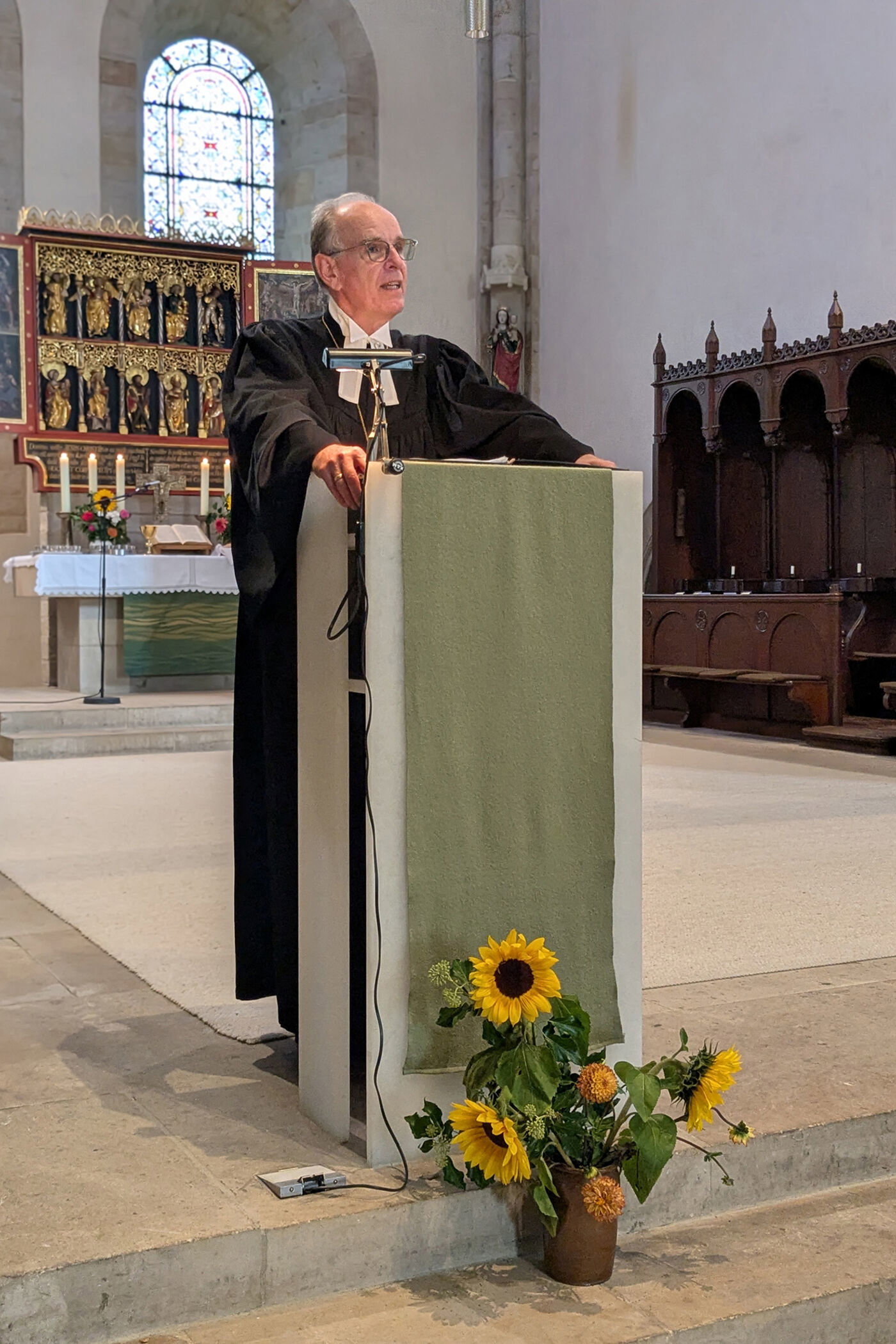 Eine als Mann lesbare Person spricht in einer Kirche an einem Redepult